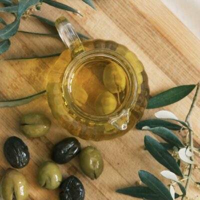 A top view of a cruet with olive oil and olives on a wooden cutting board.