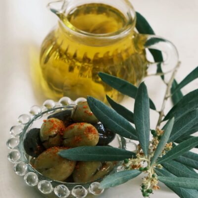 Glass jar of olive oil and plate of olives with olive branch.