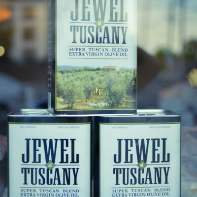 Three Jewel of Tuscany olive oil cans stacked in a window display, close-up view.